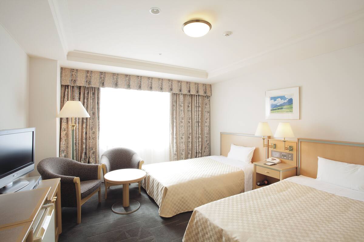 Une chambre d’hôtel avec deux lits, un bureau, une chaise, une télévision et une fenêtre avec des rideaux.