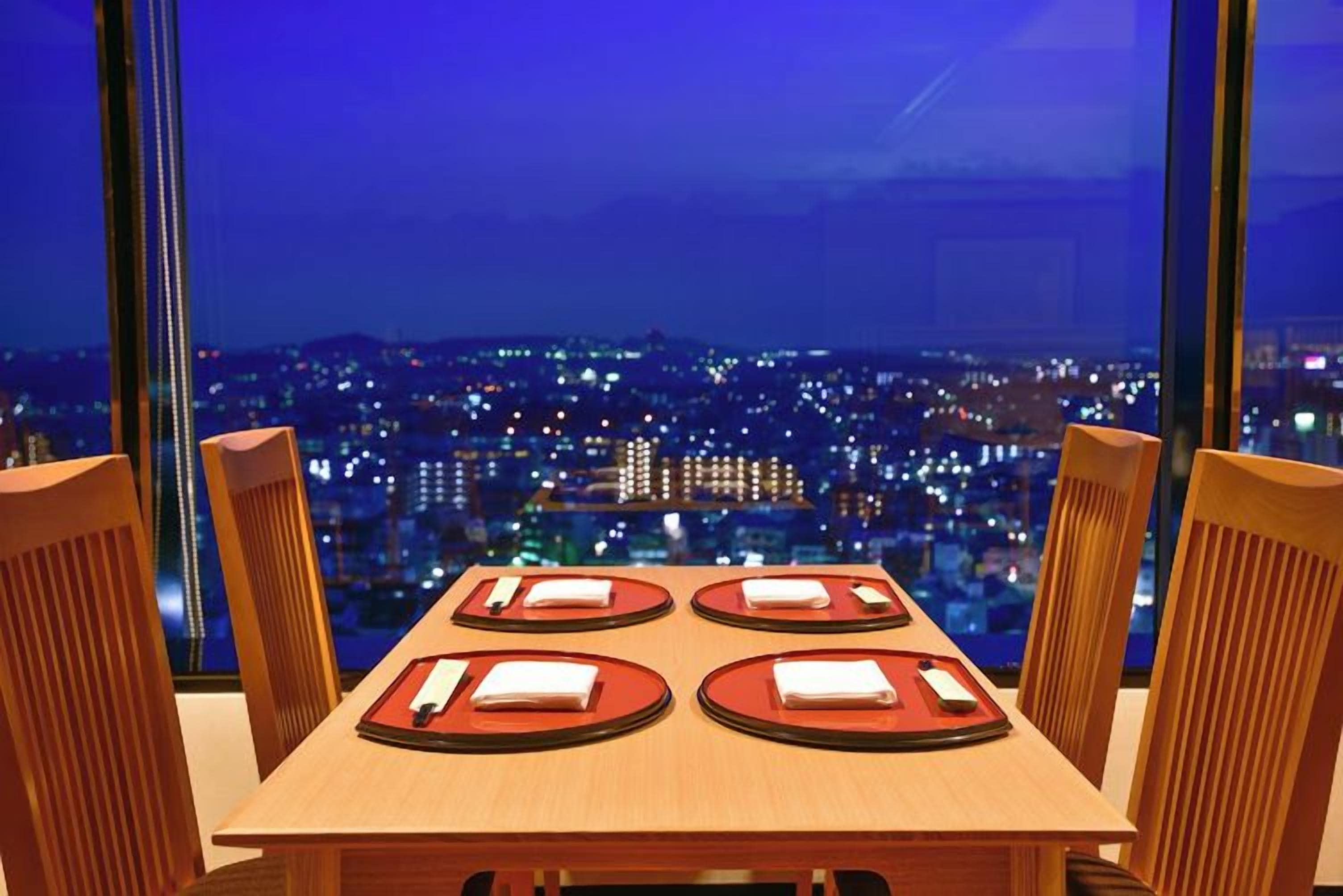 A table set for four with a cityscape view through large windows.