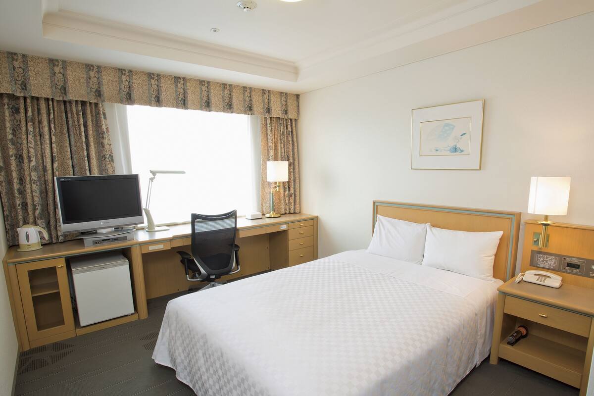 Une chambre d’hôtel équipée d’un lit, d’un bureau, d’une chaise, d’une télévision, d’une lampe et d’un petit réfrigérateur.