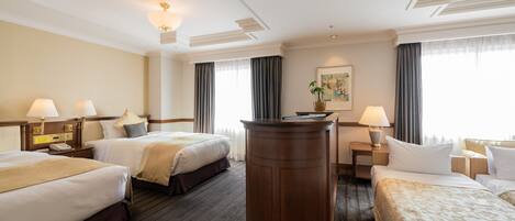 A hotel room with two beds, a desk, a chair, a large wooden desk, and a potted plant.
