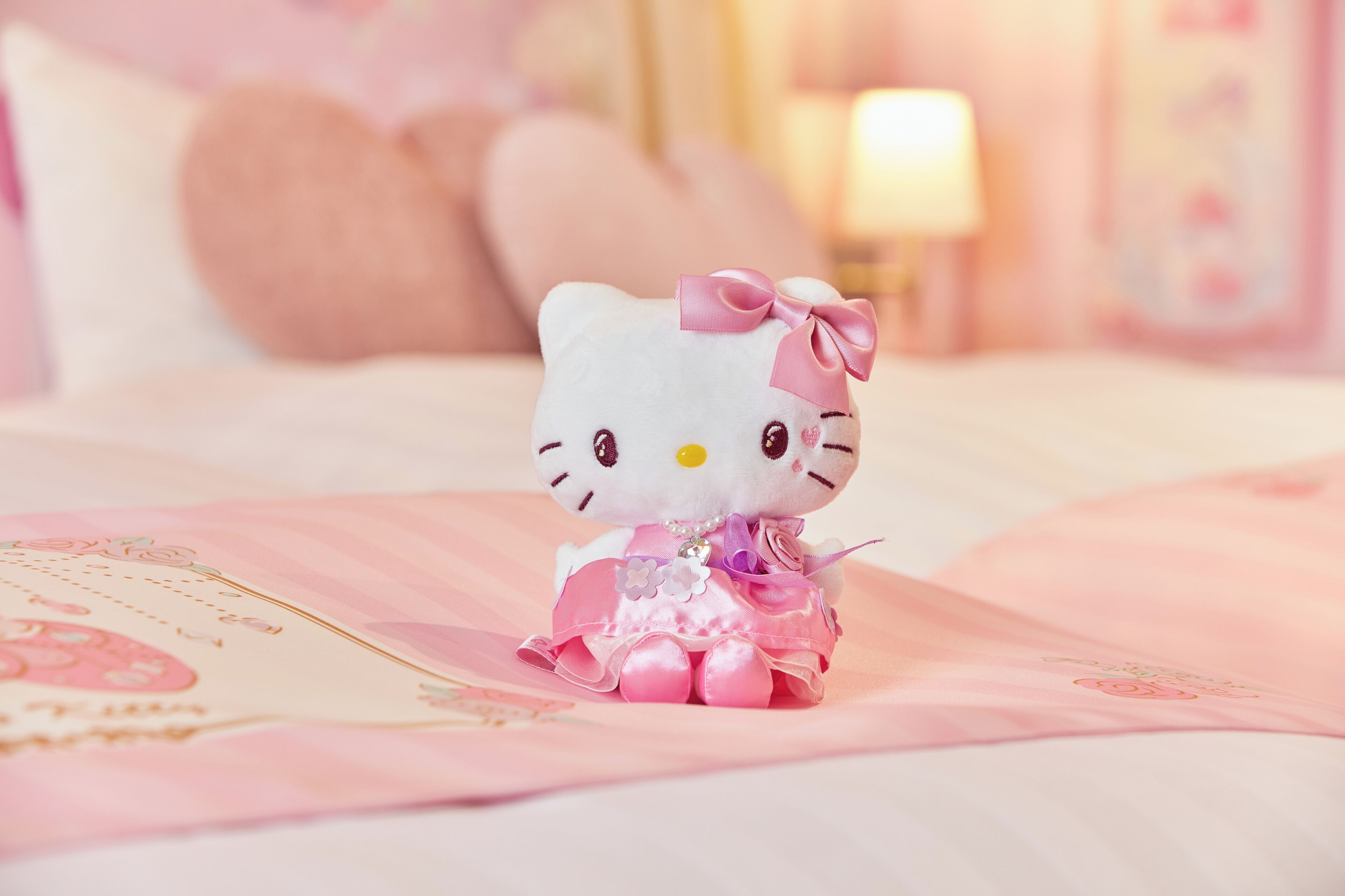 A Hello Kitty plush toy on a bed with pink bedding and pillows.