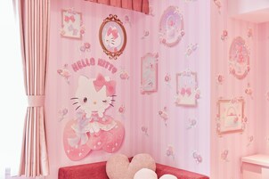 Una habitación con temática rosa, con un mural de Hello Kitty, espejos decorativos y almohadas con forma de corazón.