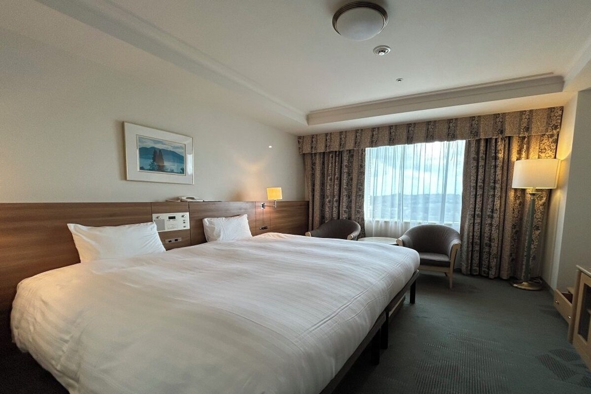 Een hotelkamer met een groot bed, een bureau, een stoel, een lamp en een raam met gordijnen.