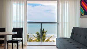 A balcony with a view of the ocean, a grey sofa, a dining table with chairs, and a colorful artwork on the wall. - Villa Varadero (Nuevo Nayarit)