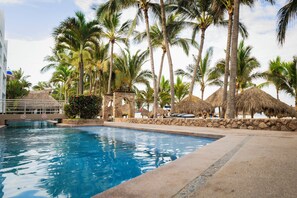 A swimming pool surrounded by palm trees and thatched-roof structures. - Villa Varadero (Nuevo Nayarit)