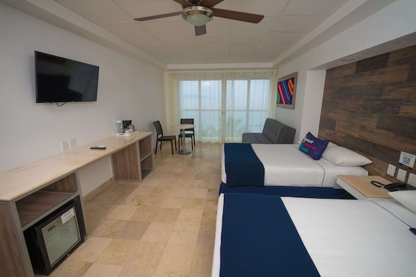 A hotel room with a flat-screen TV, a desk with a computer, two beds, a ceiling fan, and a large window with a view.