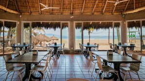 A beachside restaurant with tables and chairs, large windows, and a thatched roof. - Villa Varadero (Nuevo Nayarit)