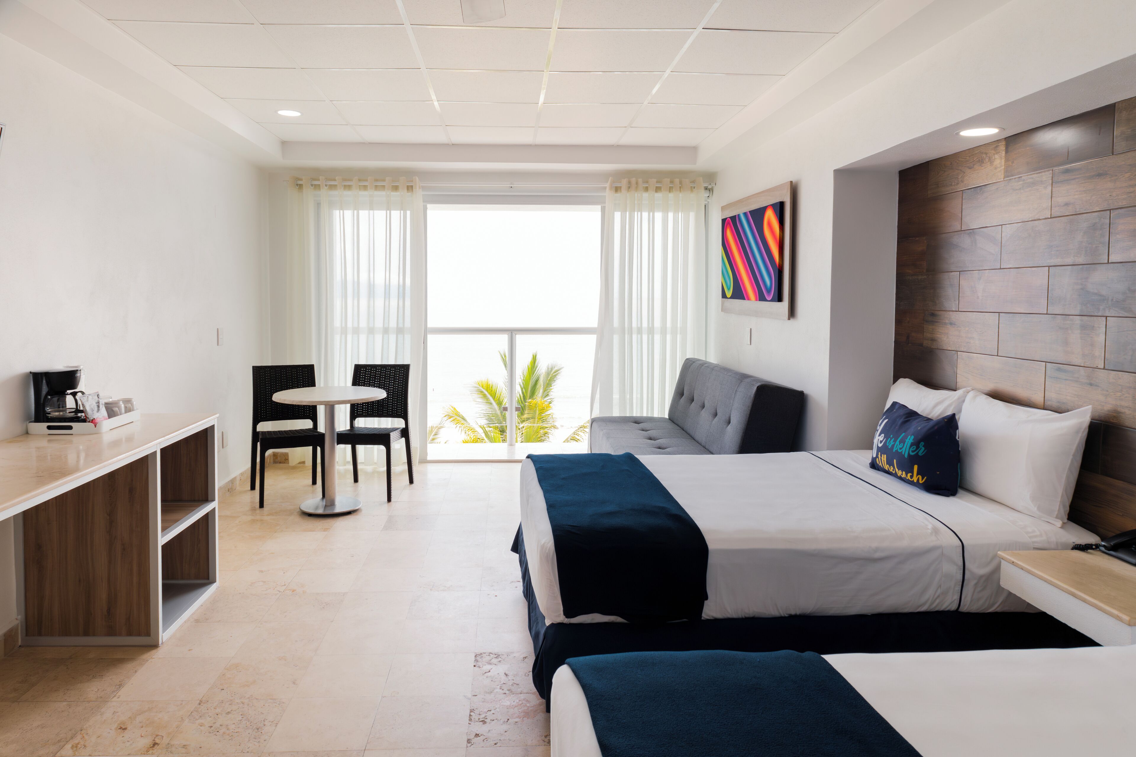 A hotel room with a bed, a desk, a chair, and a view of palm trees.