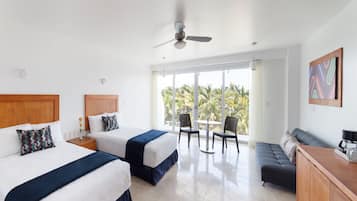 Quarto de hotel com duas camas, um sofá, uma mesa de jantar e vista para palmeiras.