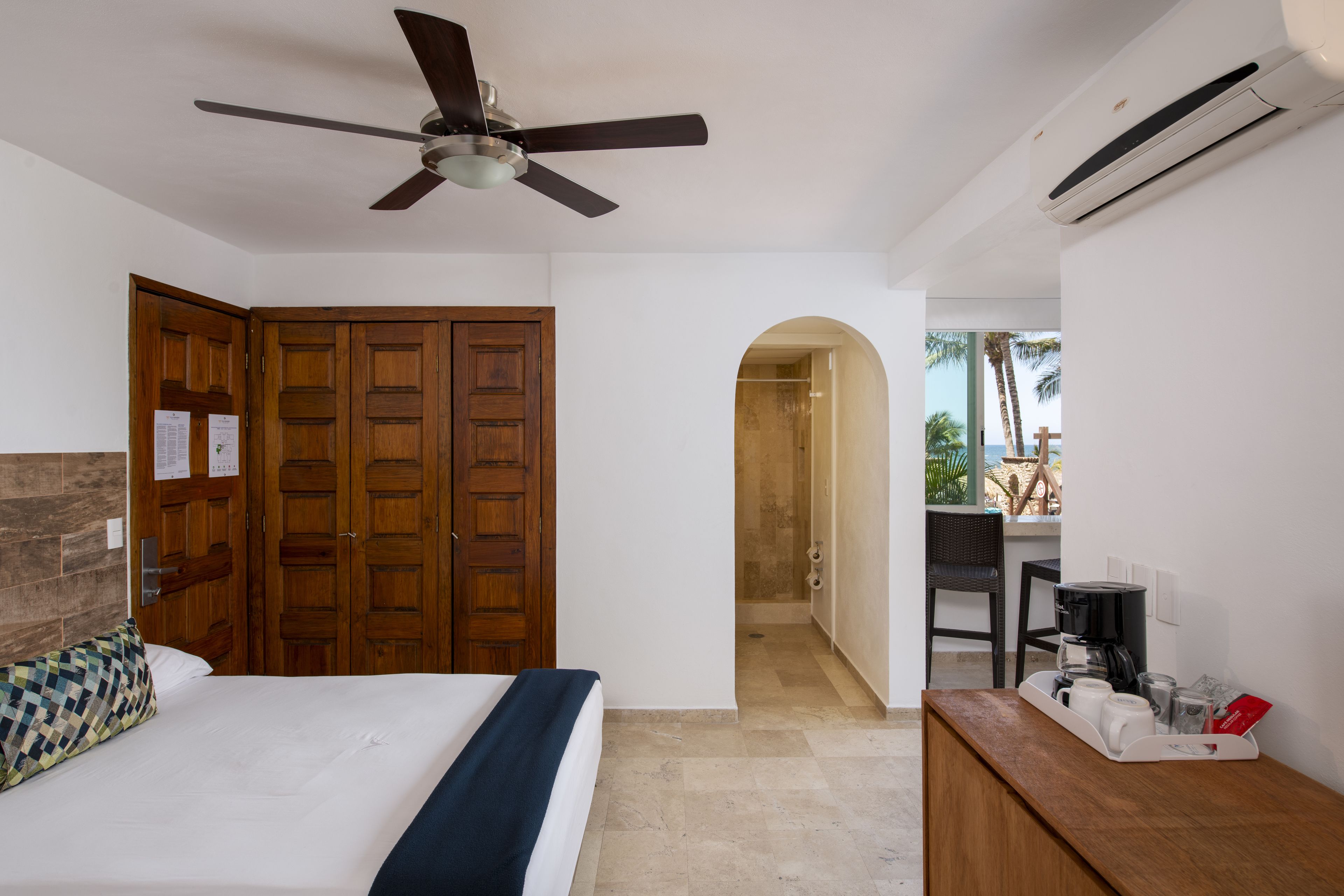 Une chambre d’hôtel équipée d’un lit, d’un ventilateur de plafond, d’une armoire en bois, d’un bureau avec une machine à café et d’un appareil de climatisation.
