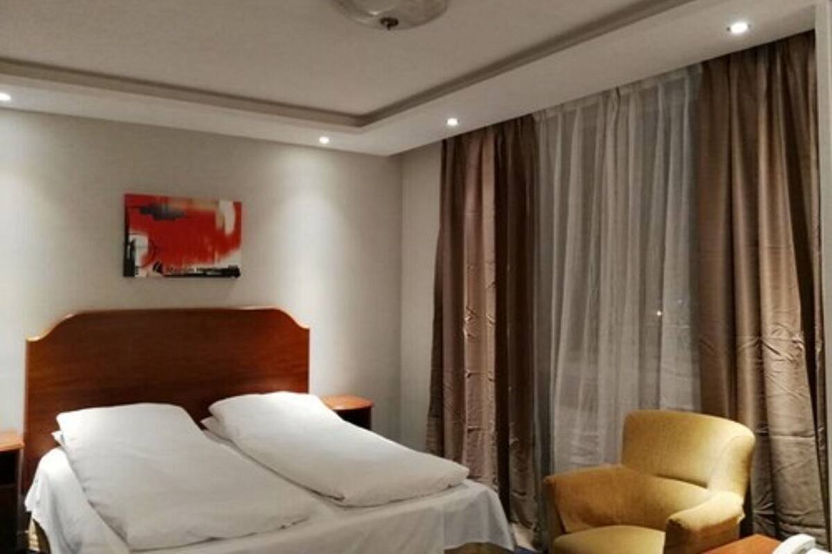 Et hotelværelse med en seng, en lænestol, et natbord, et billede på væggen og et vindue med gardiner.