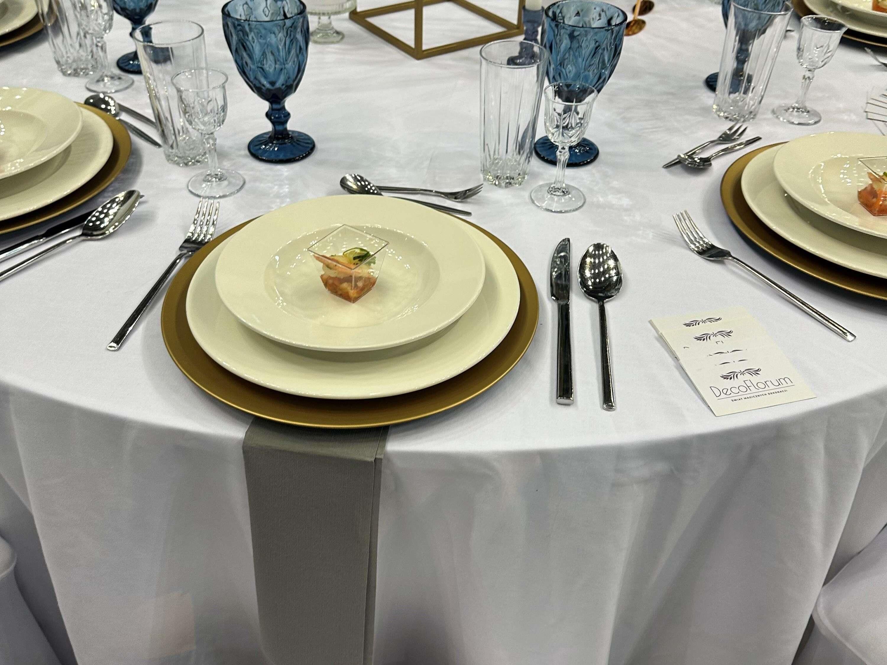 Une table ronde dressée avec des assiettes, des couverts et un menu.