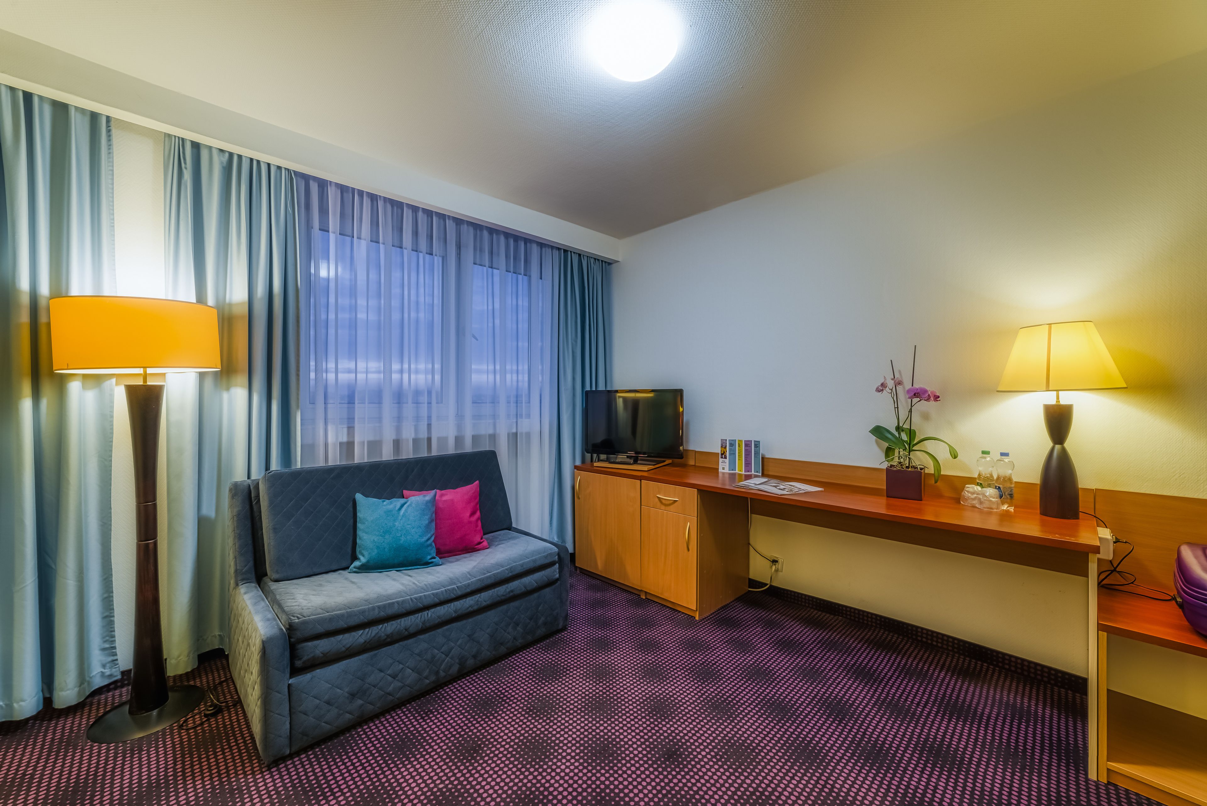 Una habitación de hotel con sofá, escritorio, televisión y lámpara.
