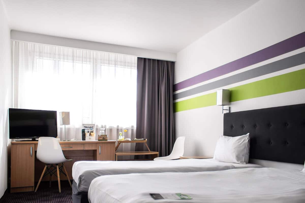 A hotel room with two beds, a desk, a television, and a window with curtains.