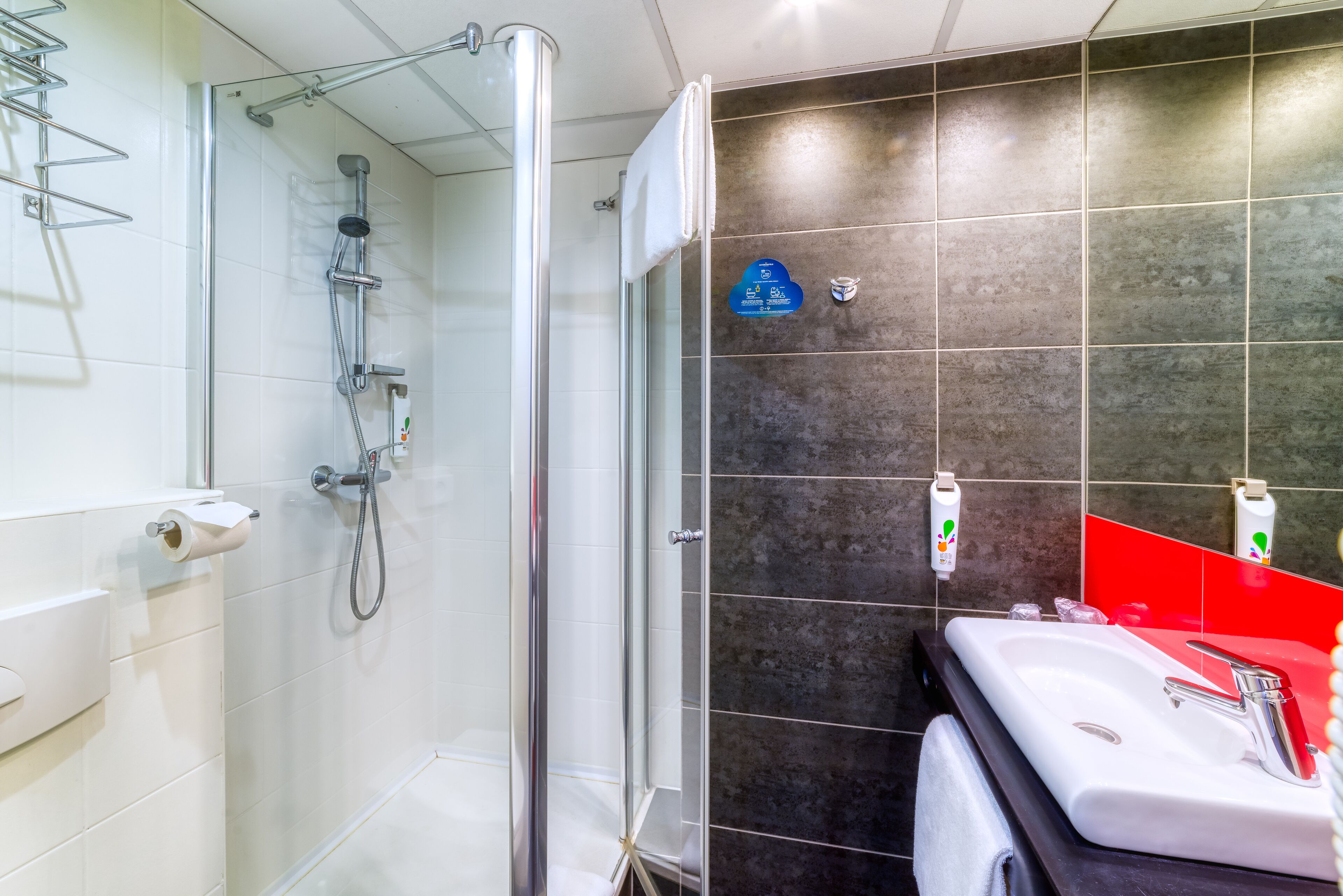 A modern bathroom with a glass-enclosed shower, a white sink with a red countertop, and dark tiled walls.