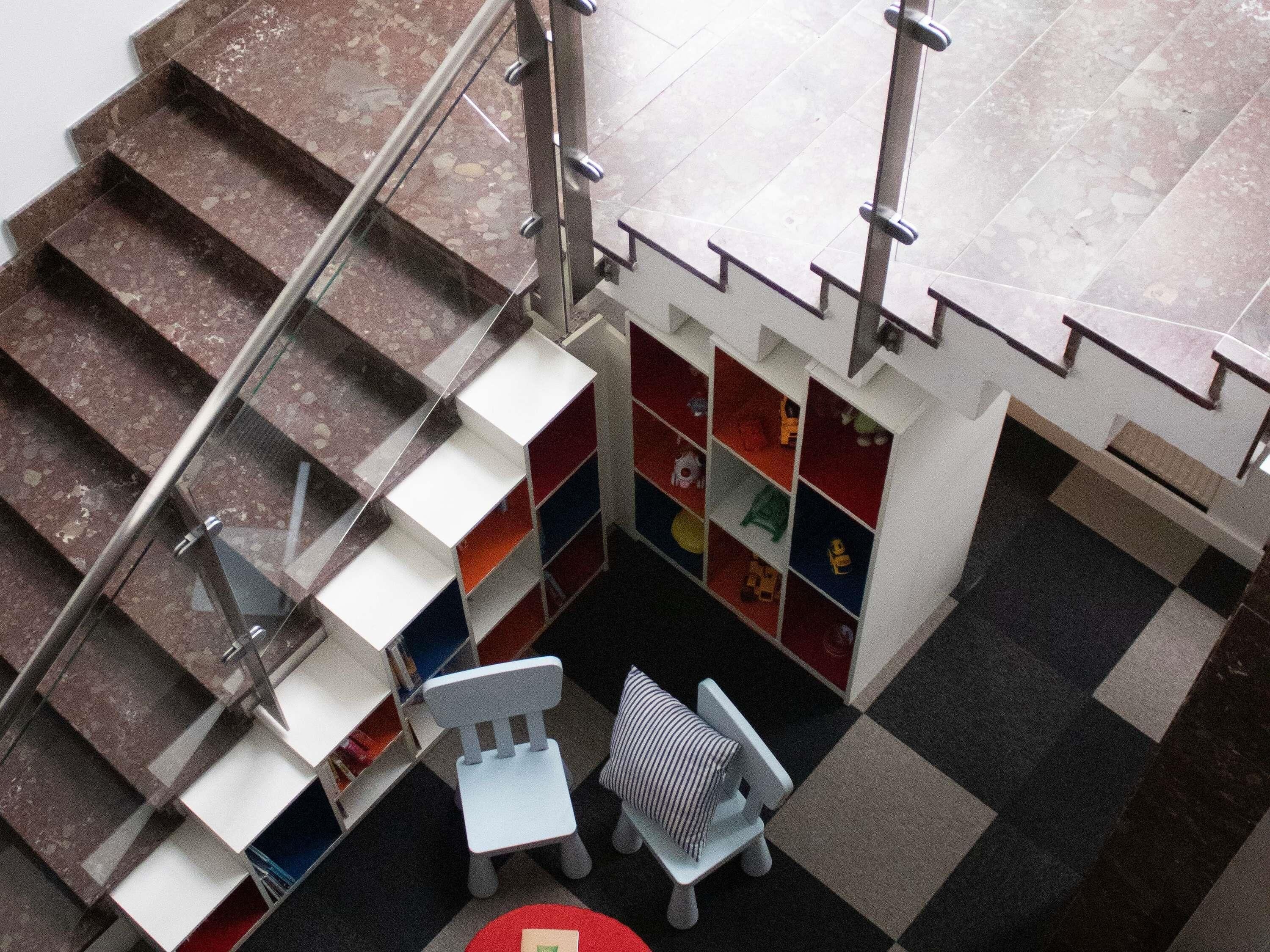A staircase with a metal railing, a small seating area with a red table, and a wall with colorful storage units.