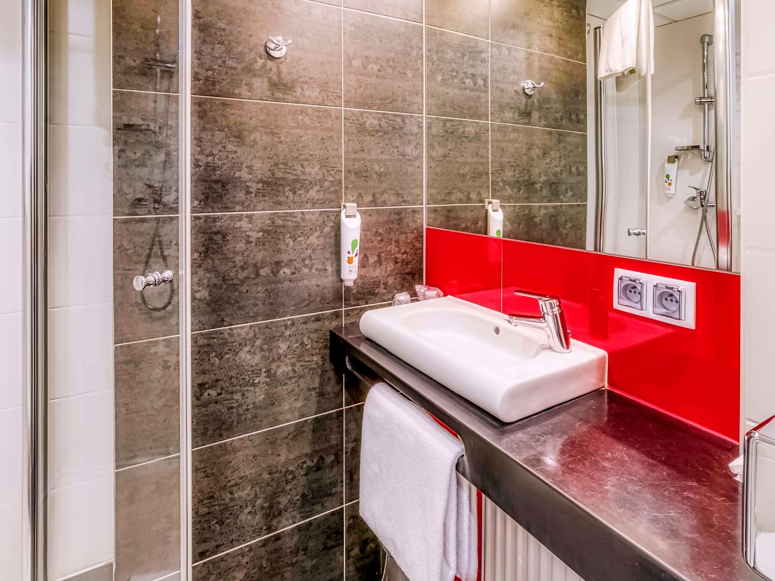 Un baño moderno con lavamanos blanco, pared de acento roja y cabina de ducha de vidrio.