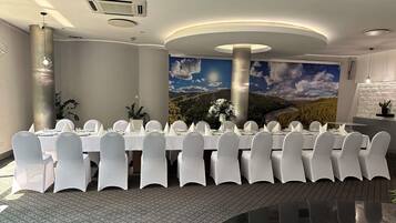 Un salón de conferencias con una larga mesa dispuesta para una reunión, rodeada de sillas, y un mural de un paisaje en la pared de fondo.