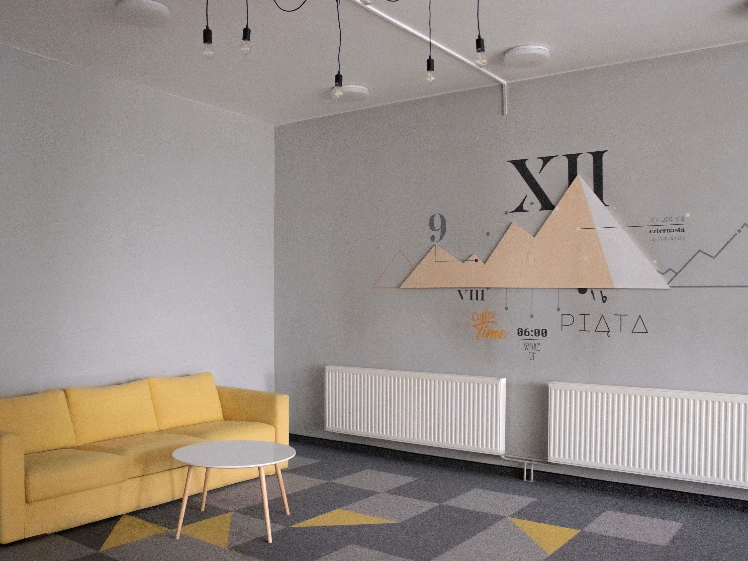 Una habitación moderna con un sofá amarillo, una mesita redonda y una pared con diseños geométricos y texto.