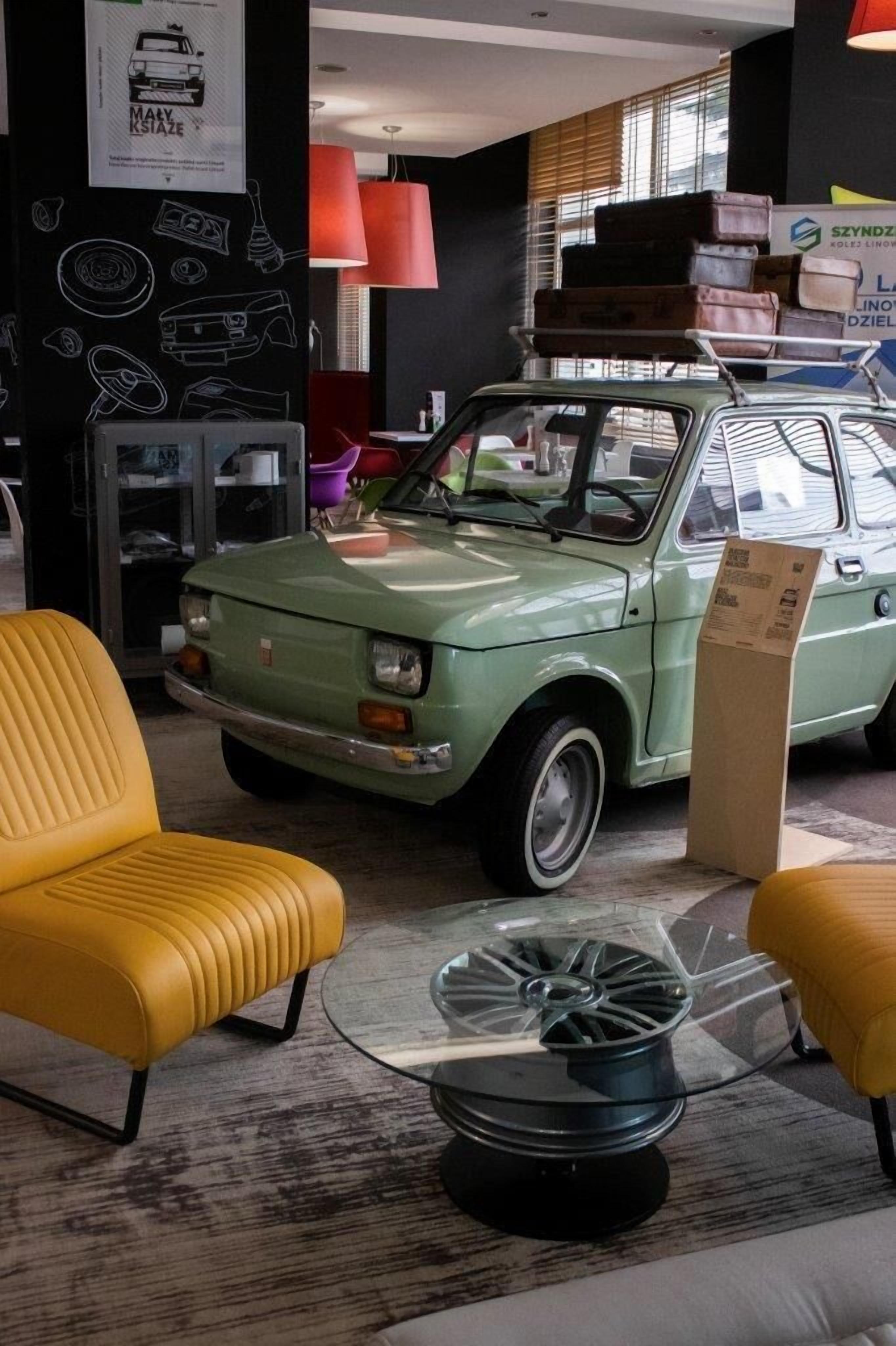 Un coche antiguo en un interior moderno con sillas amarillas y una mesa de vidrio.