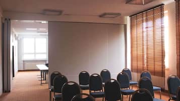 Ein Konferenzraum mit Reihen von Stühlen, einer großen Projektionsleinwand und einem Fenster mit Jalousien.