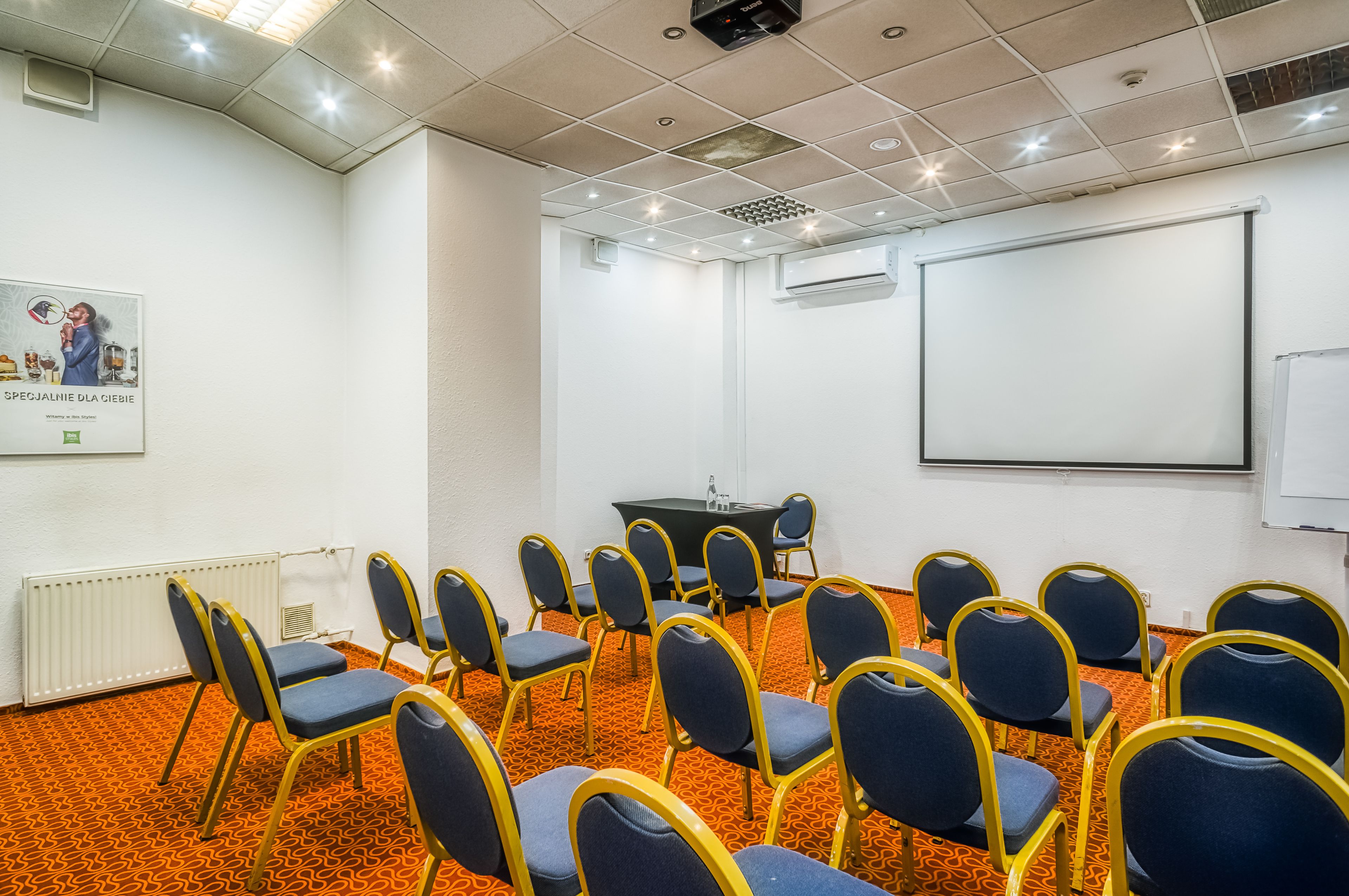 A conference room with rows of chairs, a projector screen, and a whiteboard.