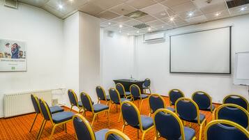 Un salón de conferencias con filas de sillas, una pantalla de proyector y una pizarra.