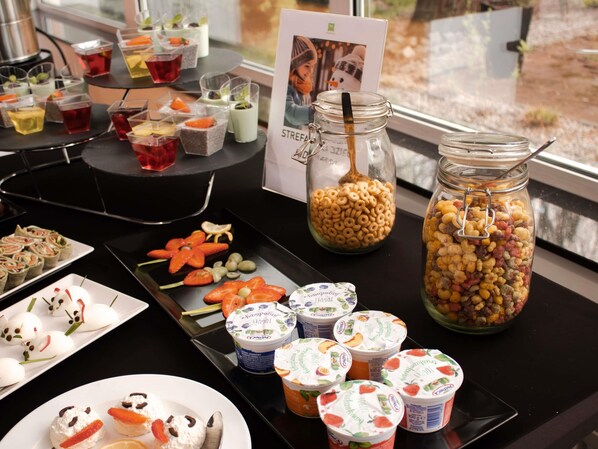 Una mesa de buffet con diversos alimentos, incluyendo vasos de yogur, cereales y brochetas de fruta.