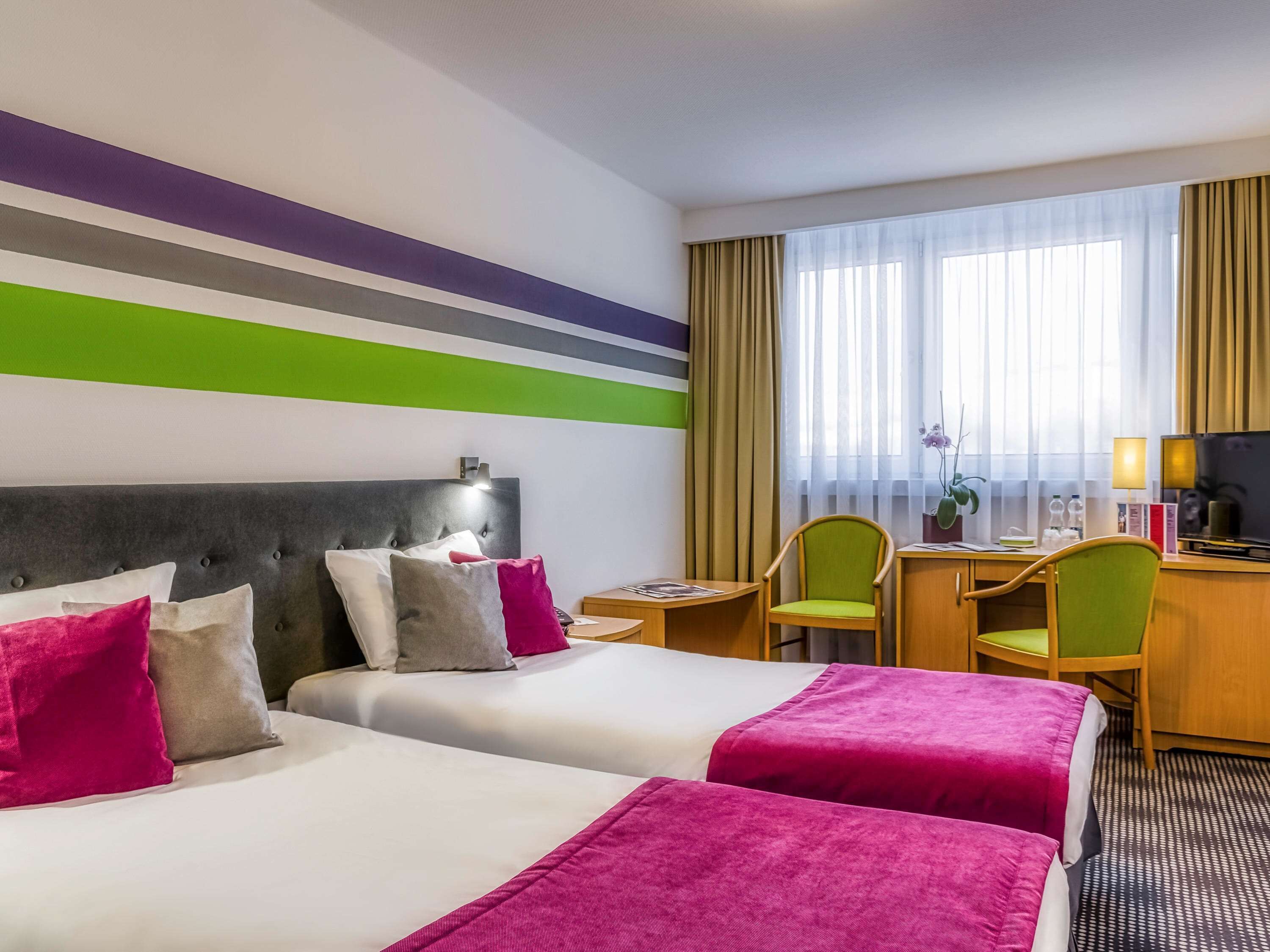 A hotel room with two beds, a desk, a chair, and a TV.