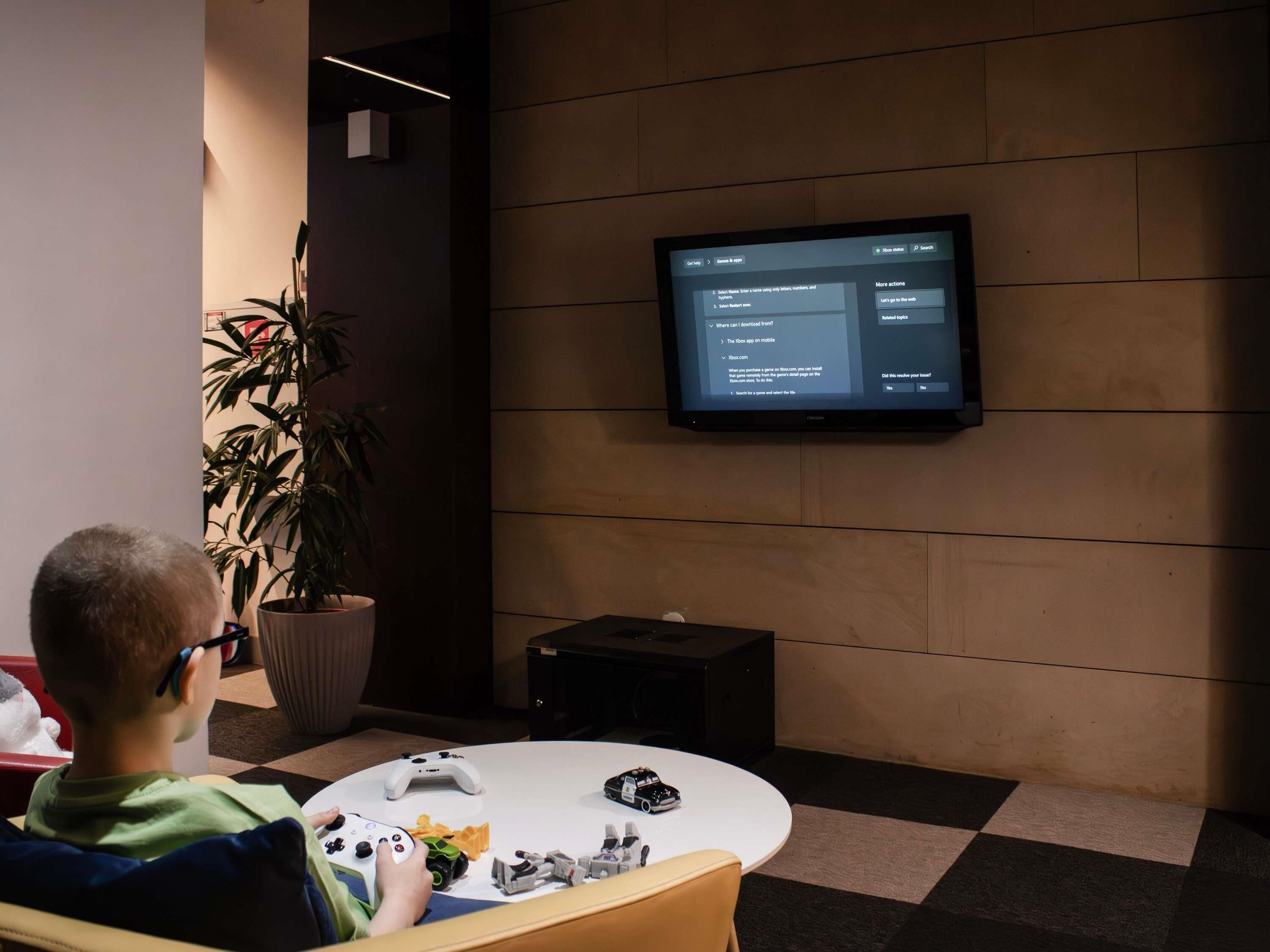 A person sitting on a chair, using a gaming console with a controller, in front of a television displaying a menu.