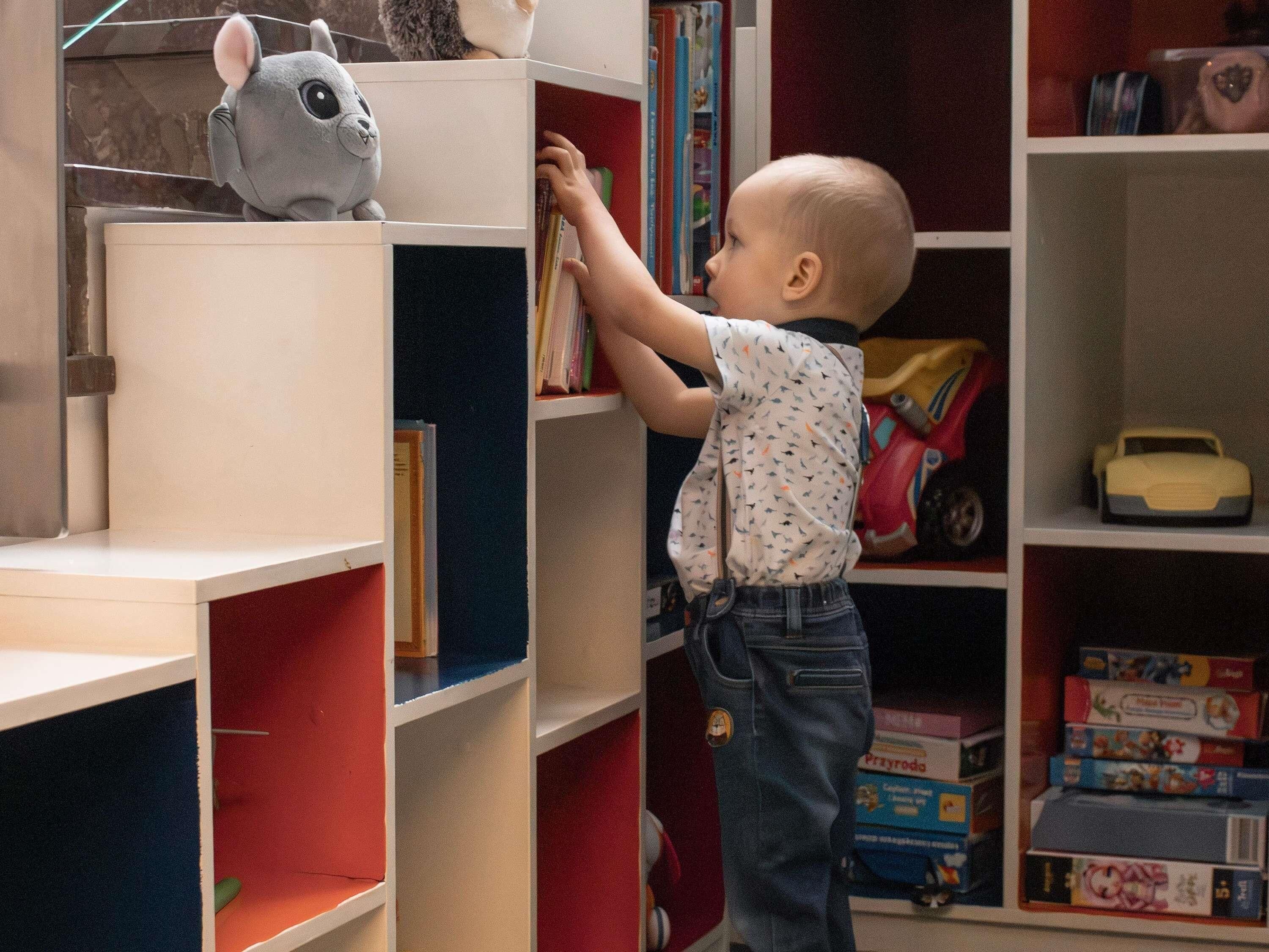 Un enfant tend la main pour attraper un livre sur une étagère.