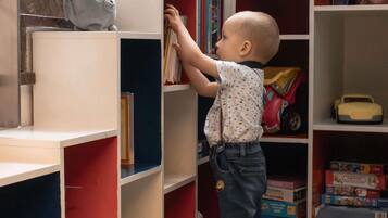 Un enfant tend la main pour attraper un livre sur une étagère.