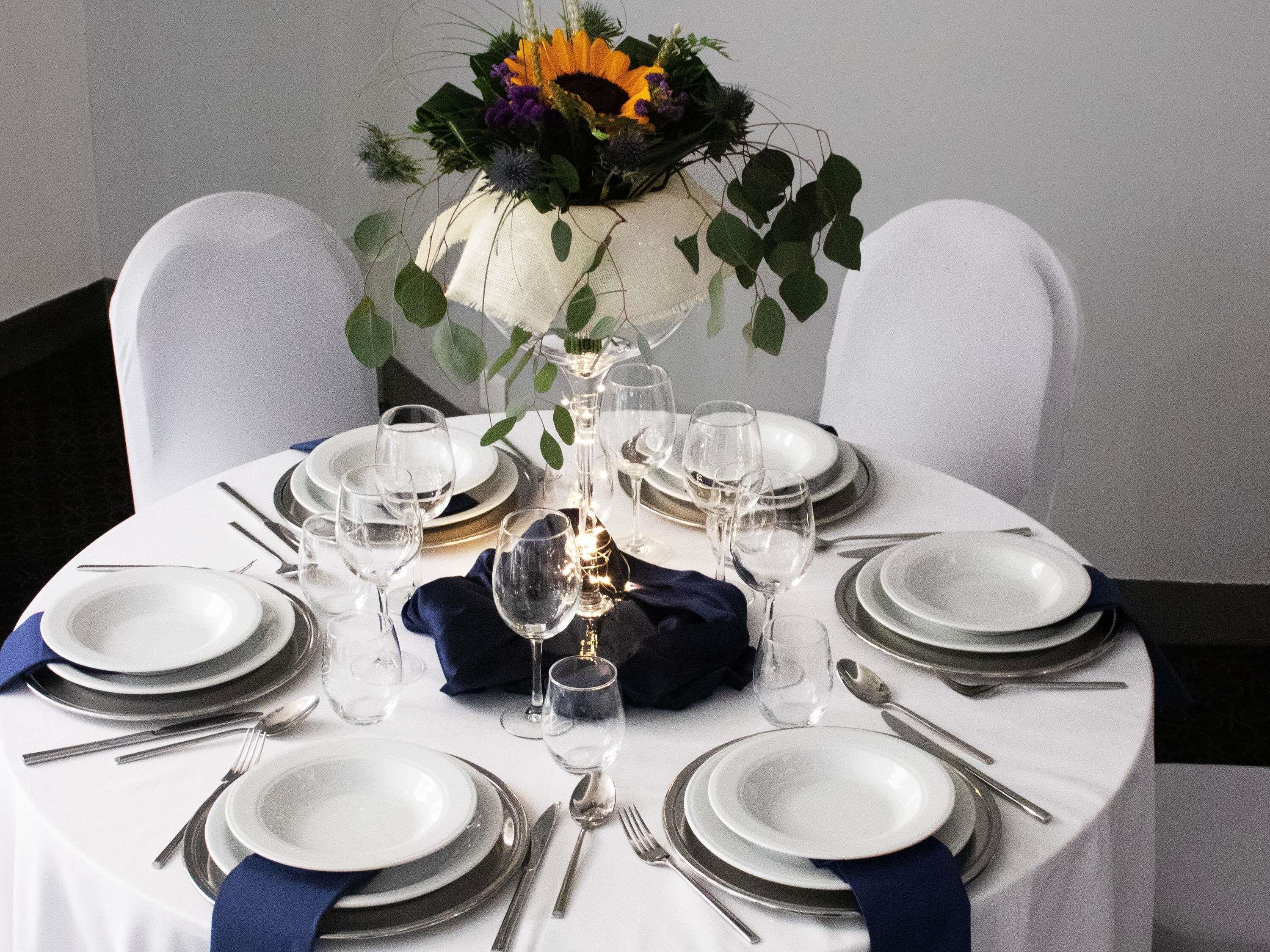 A round table set for dining with white plates, silverware, and clear glasses.