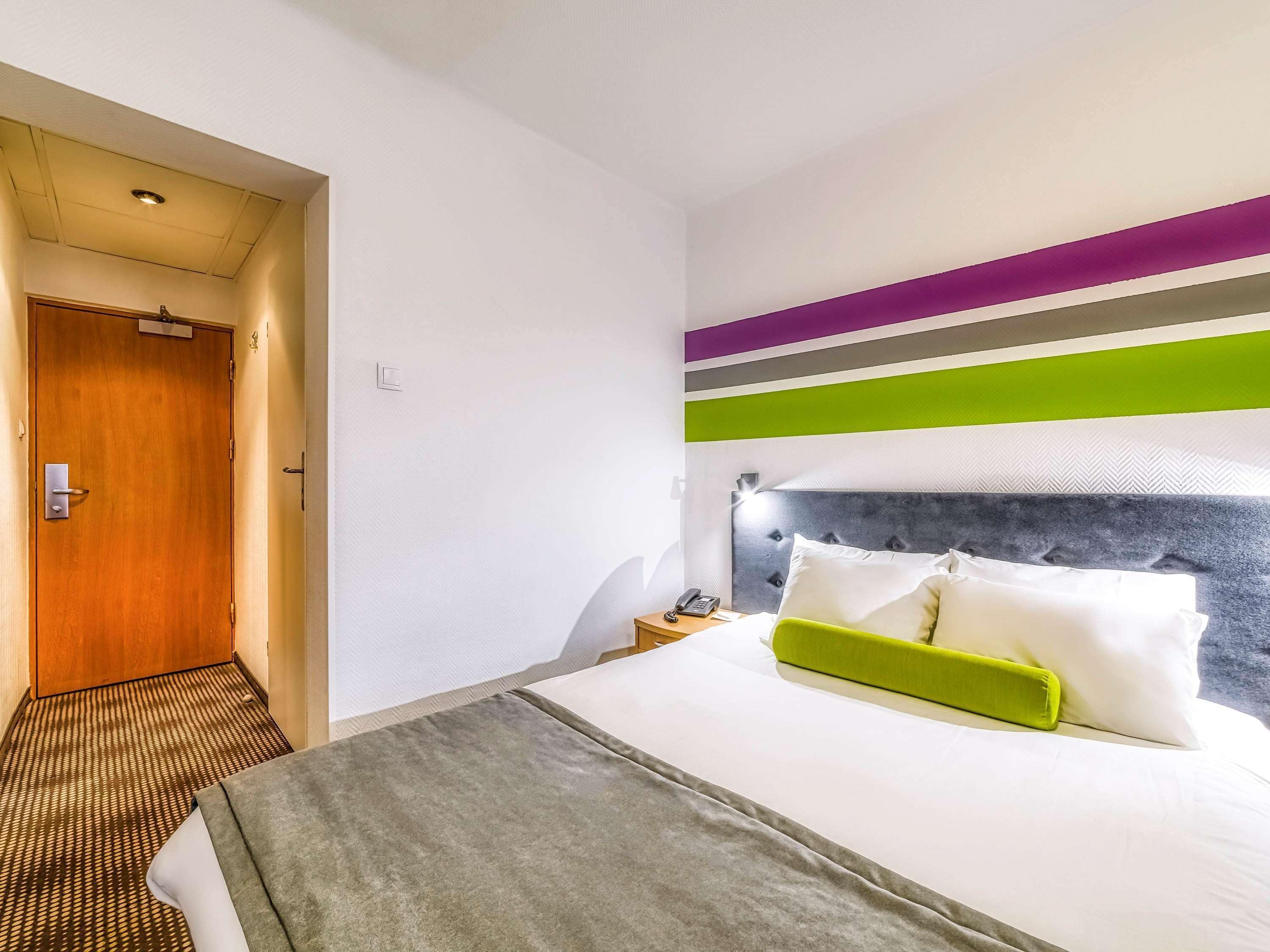 Een hotelkamer met een bed, een nachtkastje met een telefoon en een deur.
