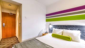 Een hotelkamer met een bed, een nachtkastje met een telefoon en een deur.