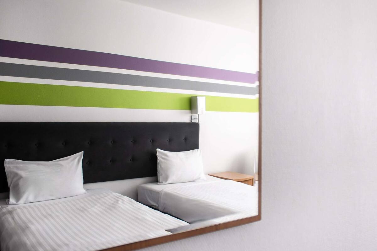 A hotel room with a bed, two pillows, a headboard, a bedside table, and a wall with horizontal stripes.