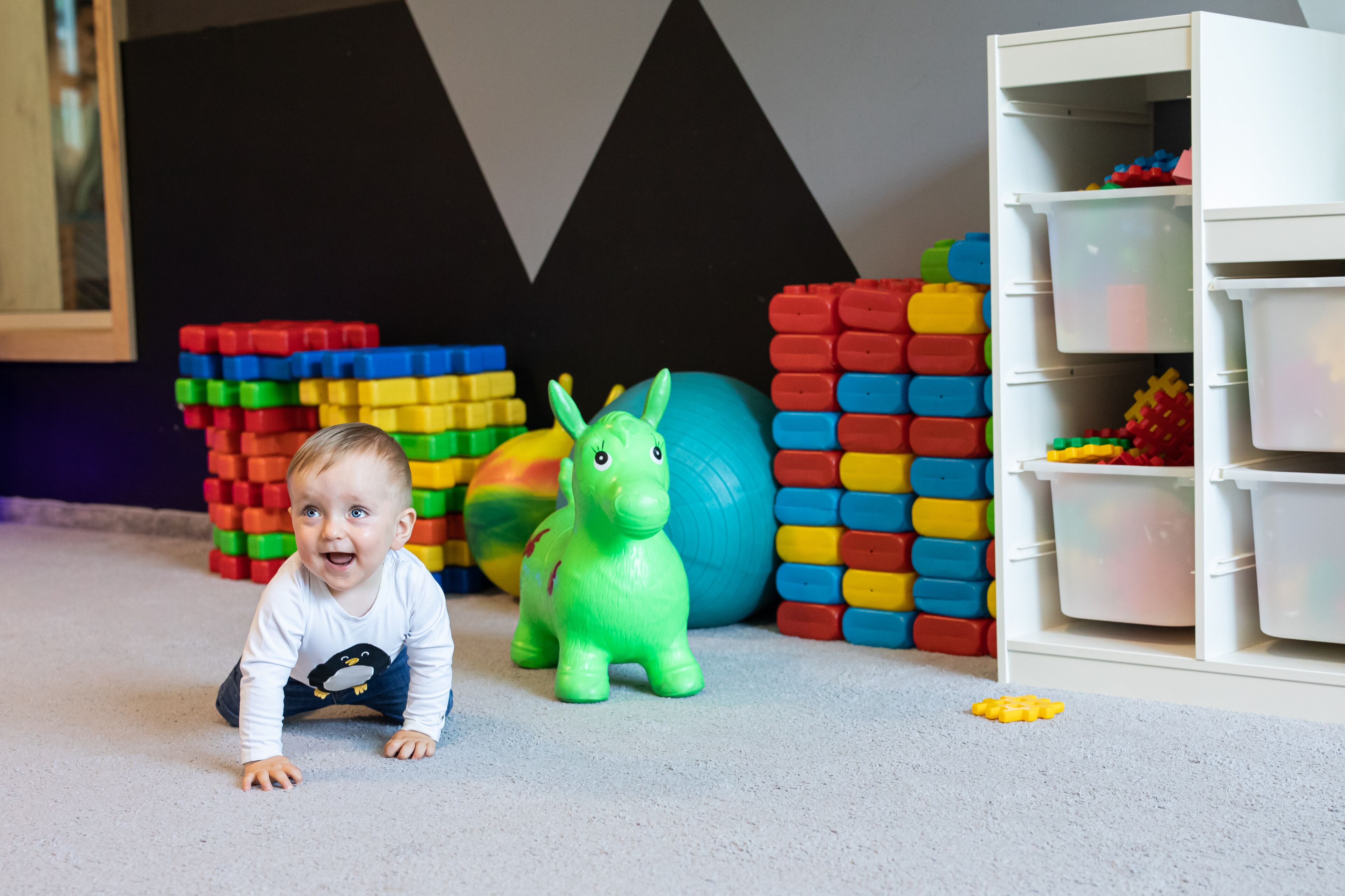 A child playing with colorful building blocks and a toy dinosaur on a carpeted floor.