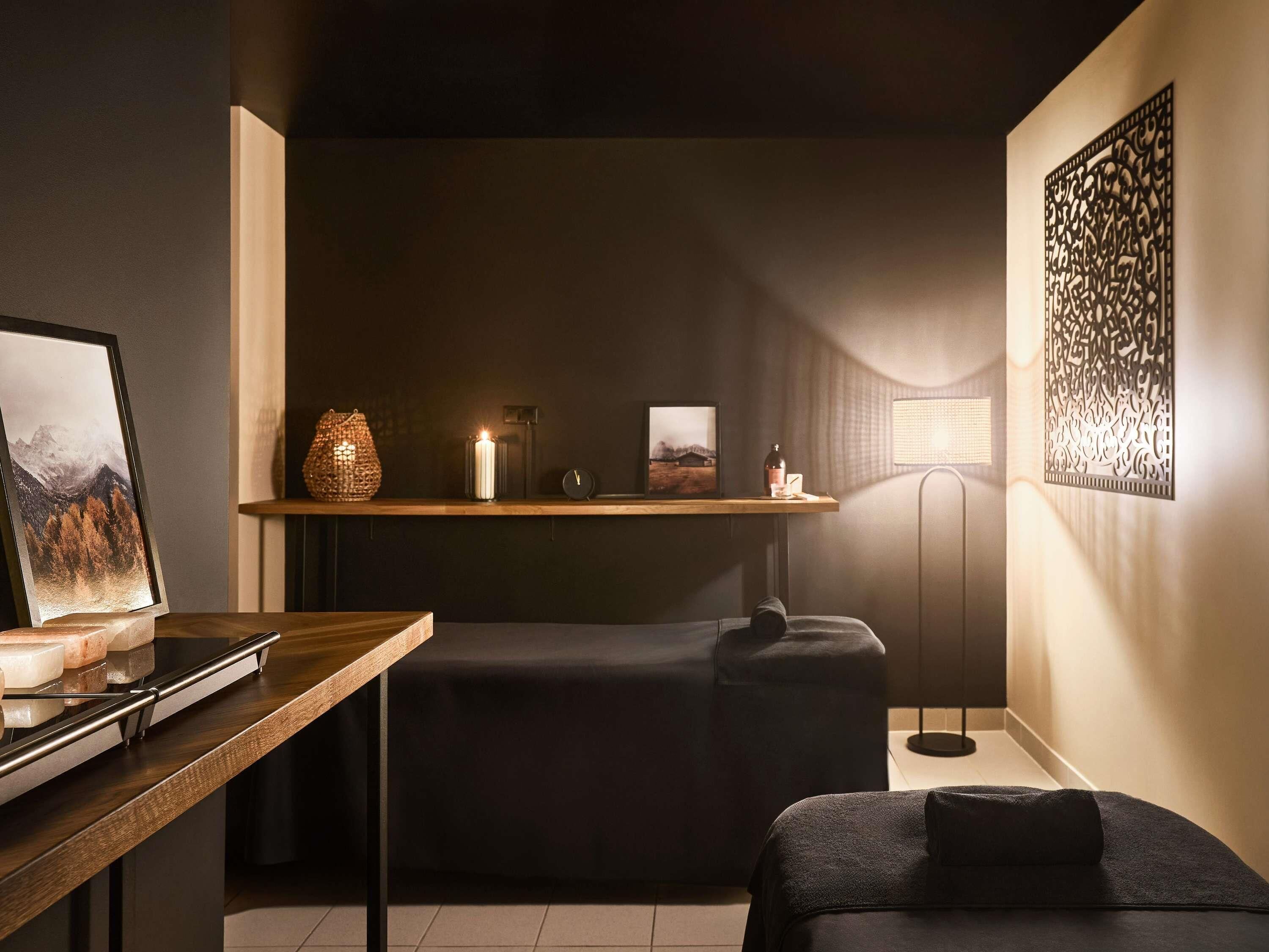 A modern room with a wooden table, a black sofa, a floor lamp, and a wall art piece.