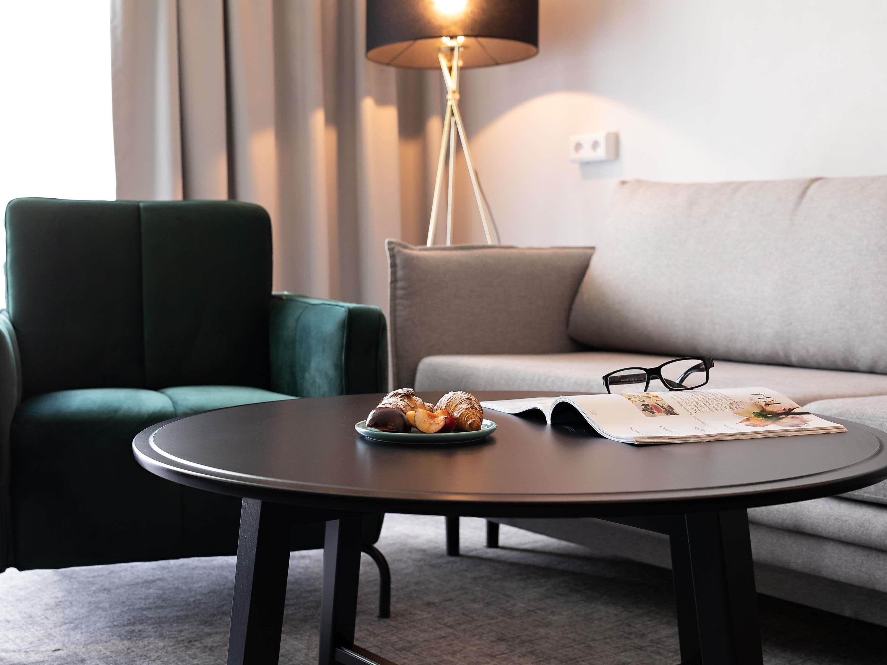 Una sala moderna con una mesa redonda, un sillón verde, un sofá gris y una lámpara de pie.