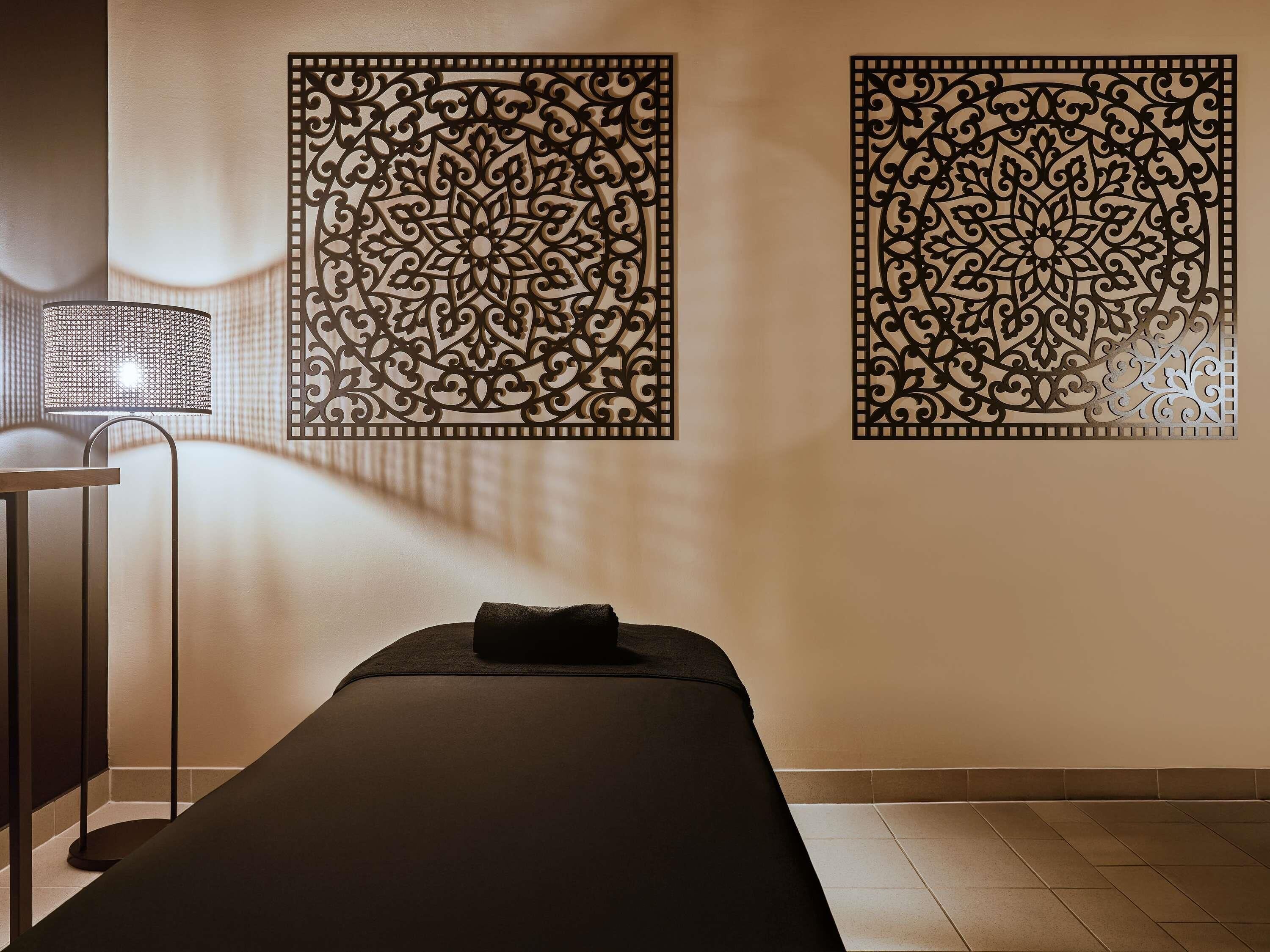 A spa room with a massage table, a wall-mounted decorative panel, and a floor lamp.