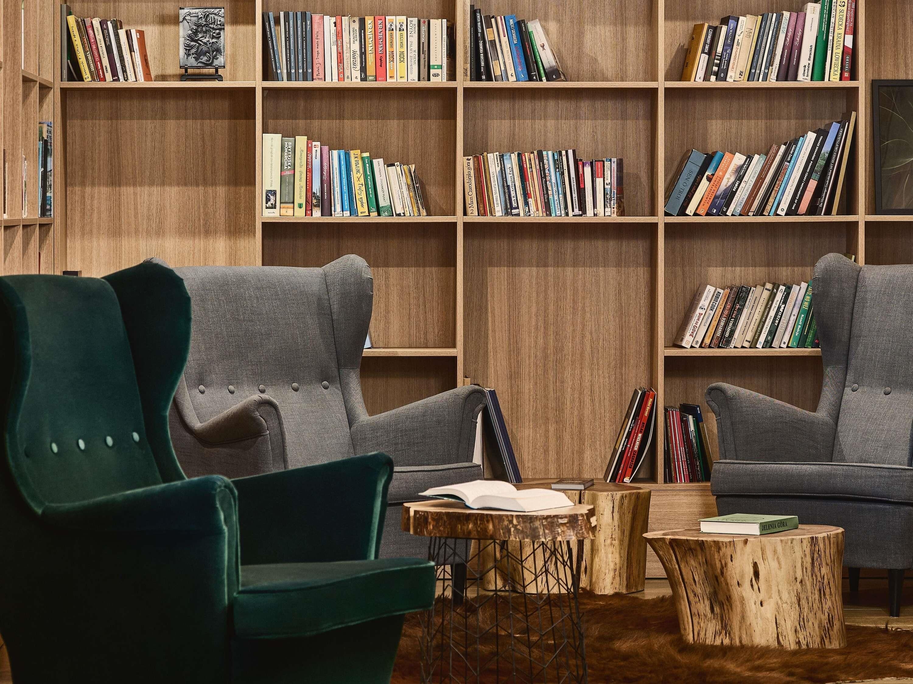A cozy reading area with two grey armchairs, a wooden bookshelf filled with books, and a small wooden table with a book on it.