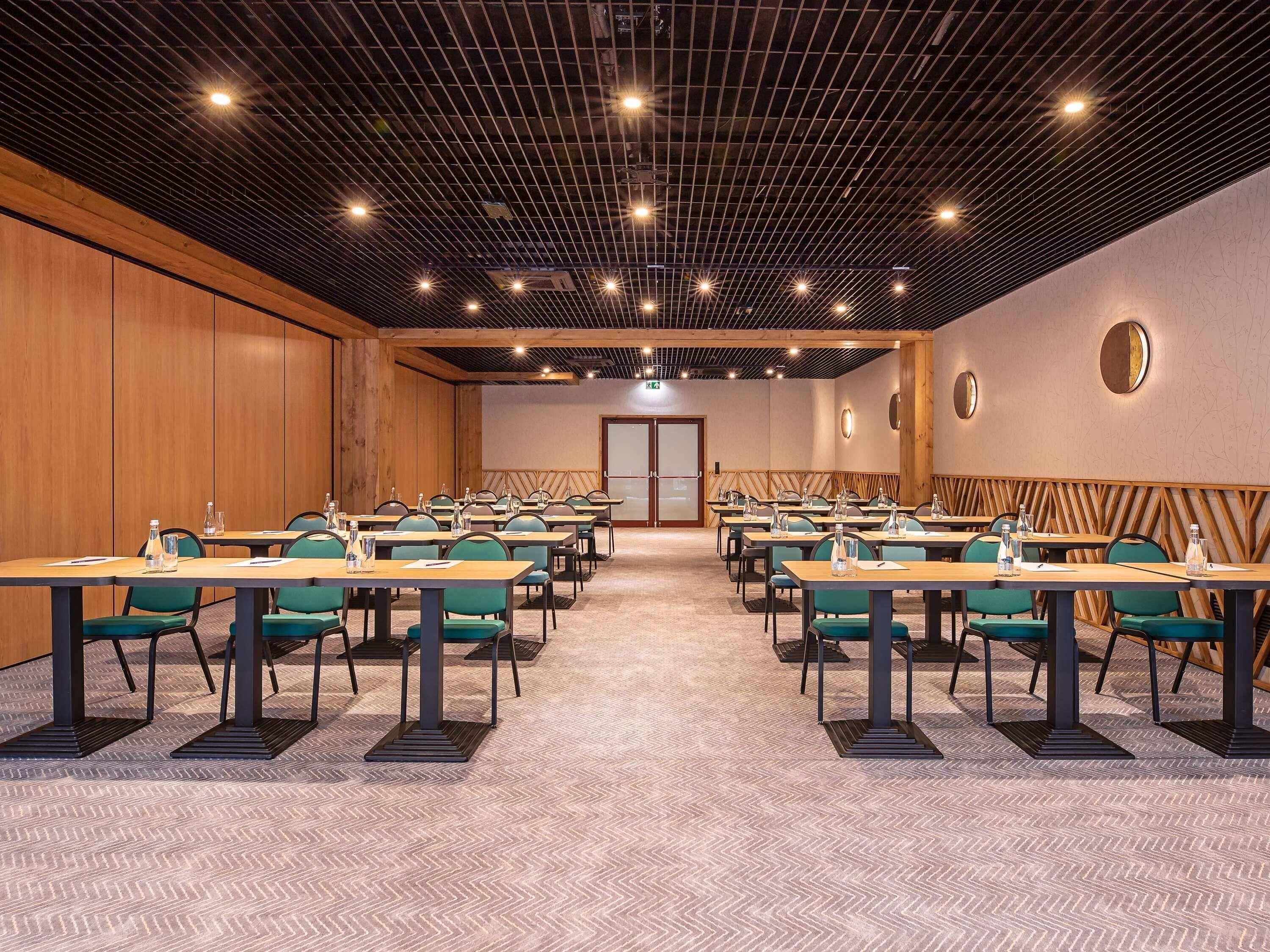 A conference room with multiple tables and chairs, a wooden panel wall, and a patterned carpet.