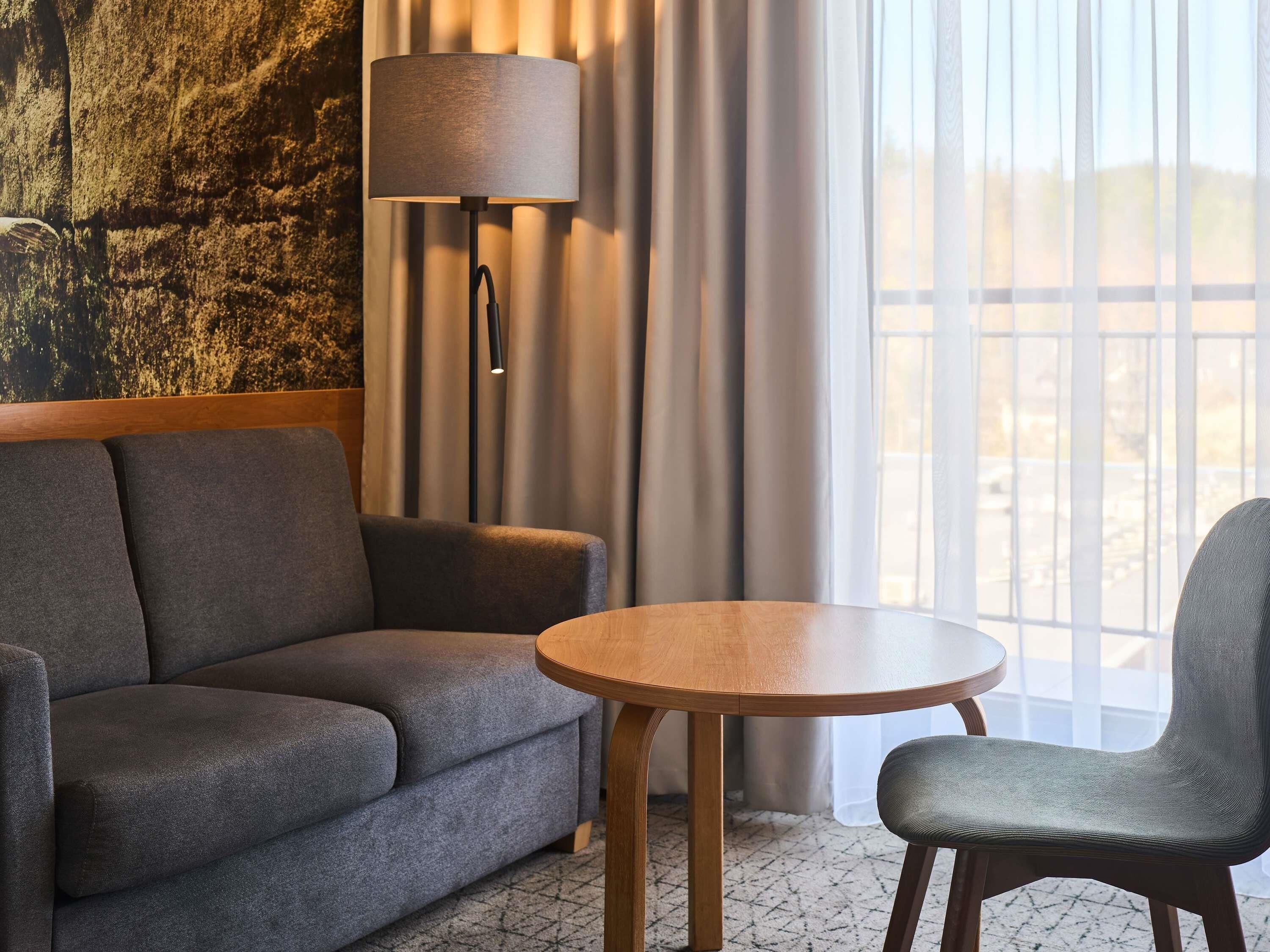 Une chambre d’hôtel moderne avec un canapé, une table ronde en bois et une chaise.