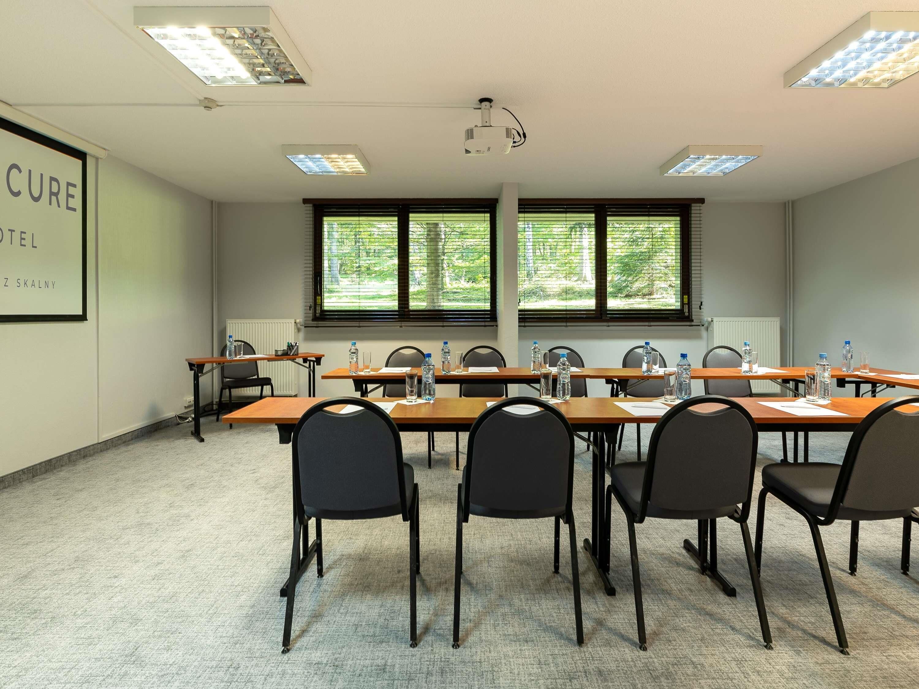 Une salle de conférence équipée d’une longue table, de chaises, d’un projecteur et de fenêtres donnant sur un paysage arboré.