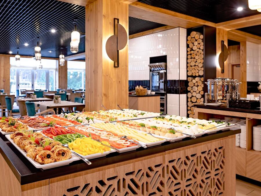 Un bufé con diversos alimentos, paneles de madera y una cocina moderna al fondo.
