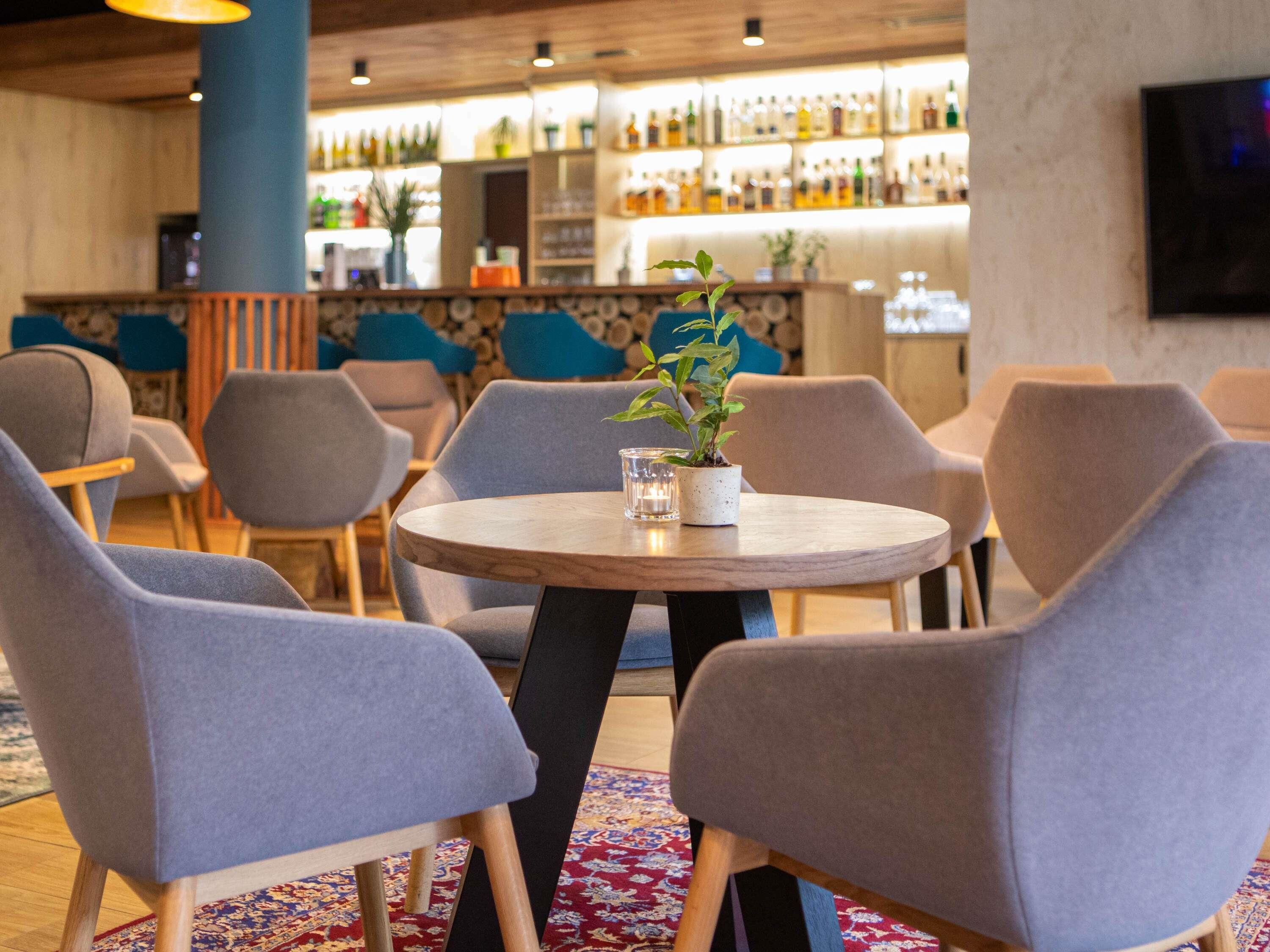 A bar area with round tables, grey upholstered chairs, and a variety of bottles on shelves.