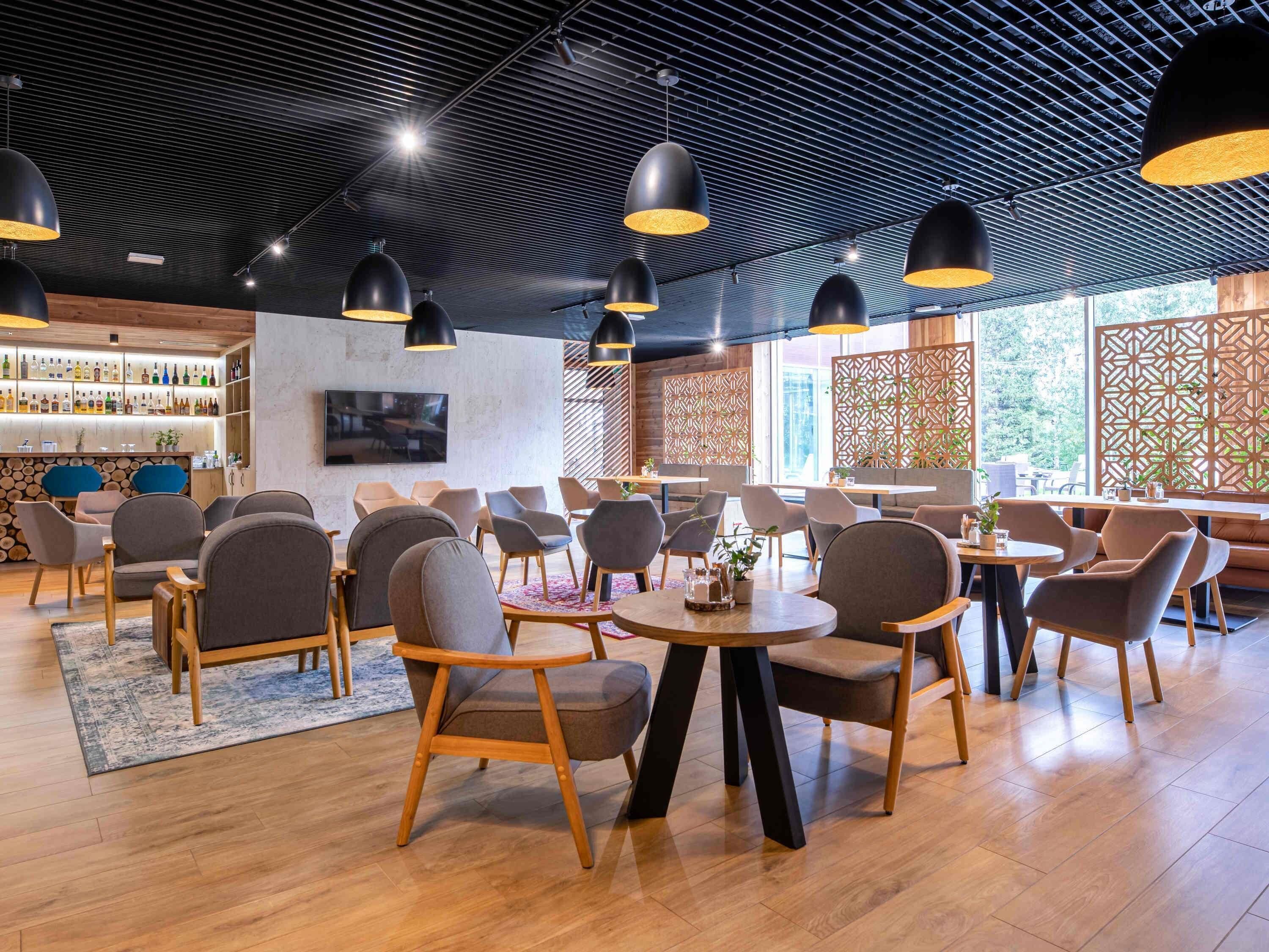 A modern bar area with wooden furniture, black pendant lighting, and a visible bar stocked with bottles.
