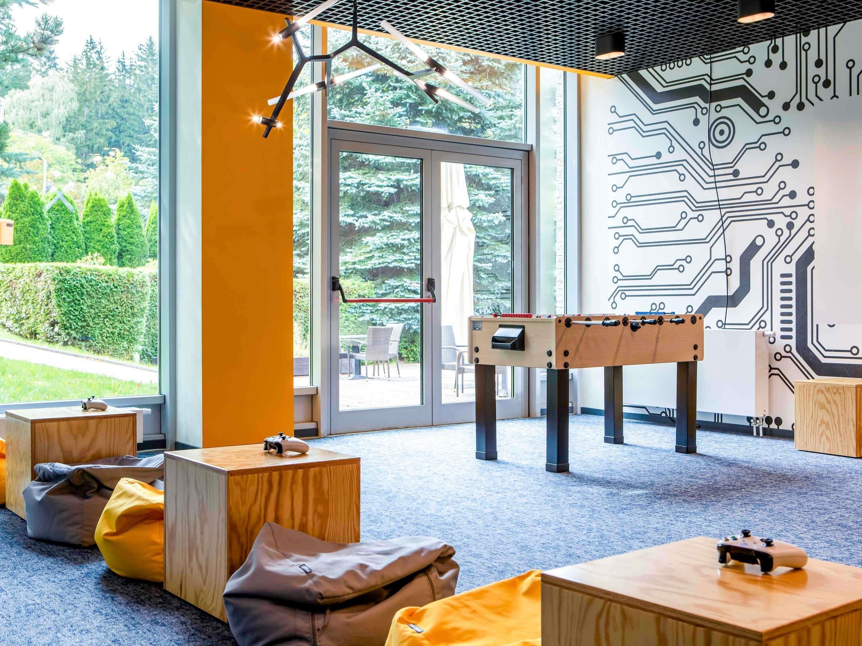 A room with a foosball table, bean bags, and a large window with a view of greenery.