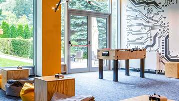 A room with a foosball table, bean bags, and a large window with a view of greenery.