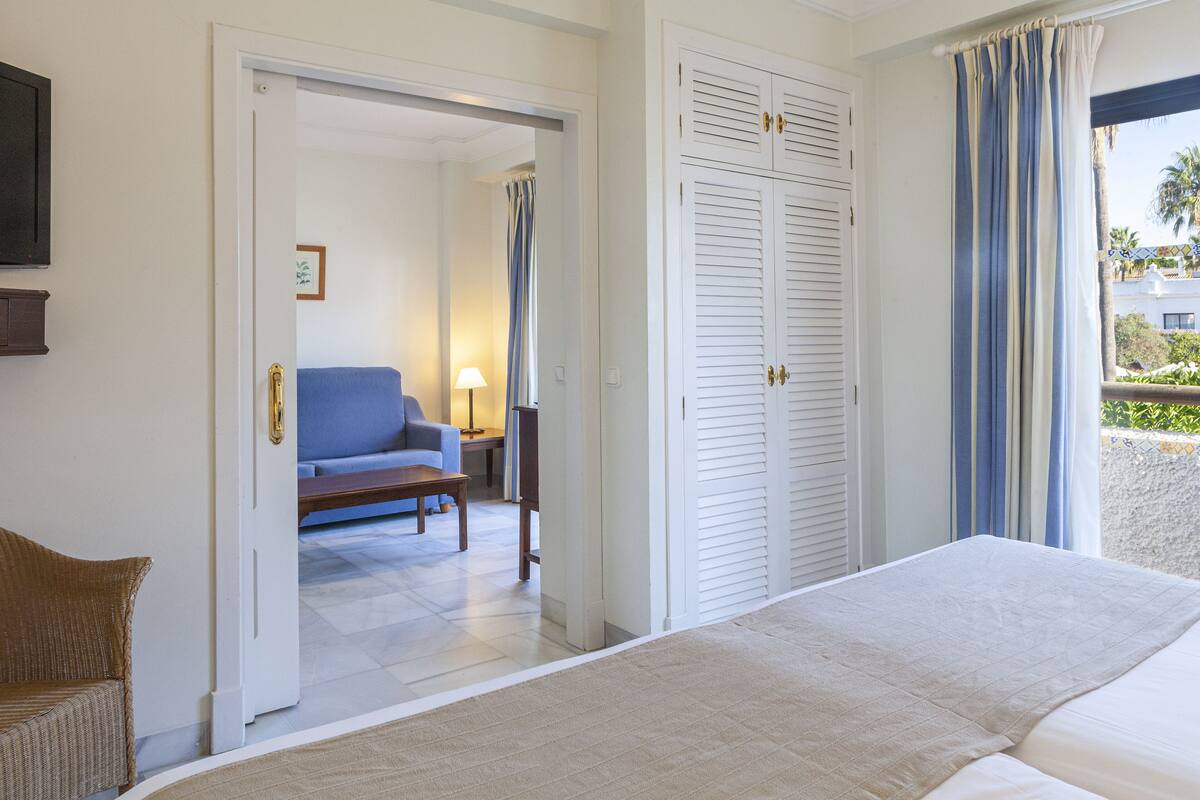Une chambre d’hôtel avec un lit, une chaise en osier, un canapé et une armoire.